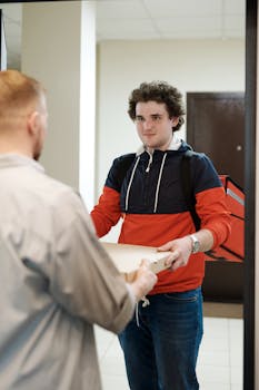 Pizza delivery person handing over a pizza box to a customer at the door.