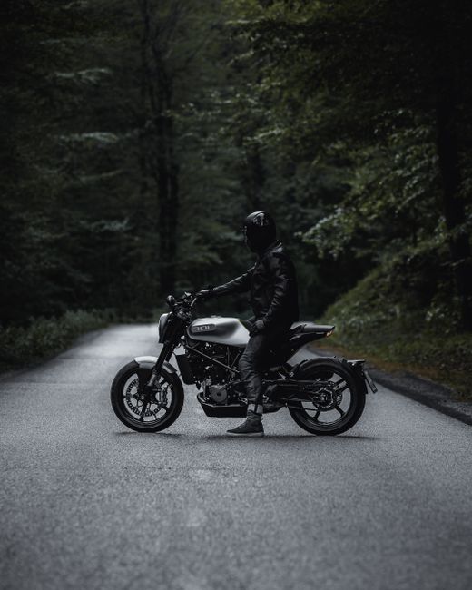 A man on a motorcycle rides down a tranquil forest road in Ljubljana, Slovenia.