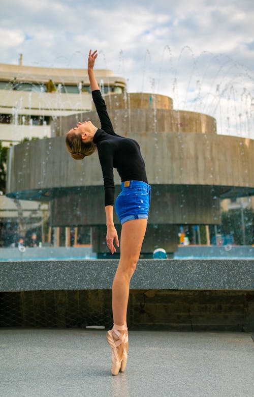 A Ballerina Standing on Her Tip Toes in front of a Fountain in City 