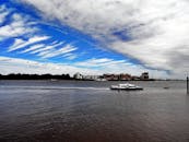 一艘渡船穿过宽阔的河流，下面是引人注目的云层，构成一个充满活力的城市场景