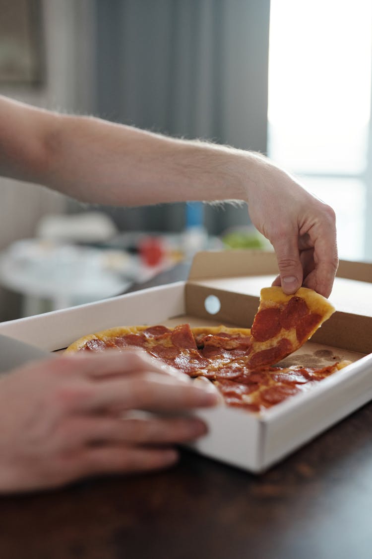 A Person Getting A Slice Of Pepperoni Pizza