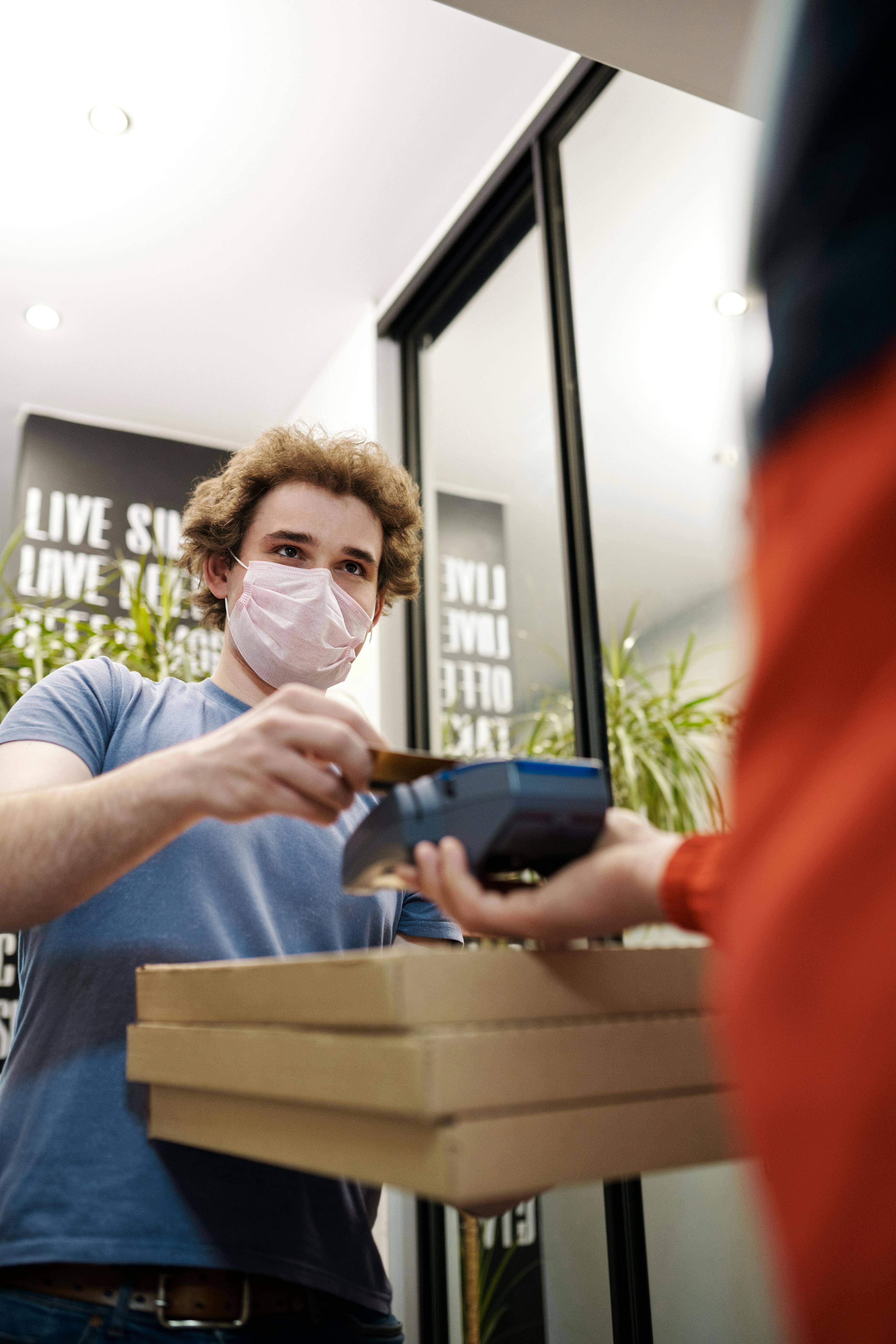 man in a face mask paying for pizza delivery