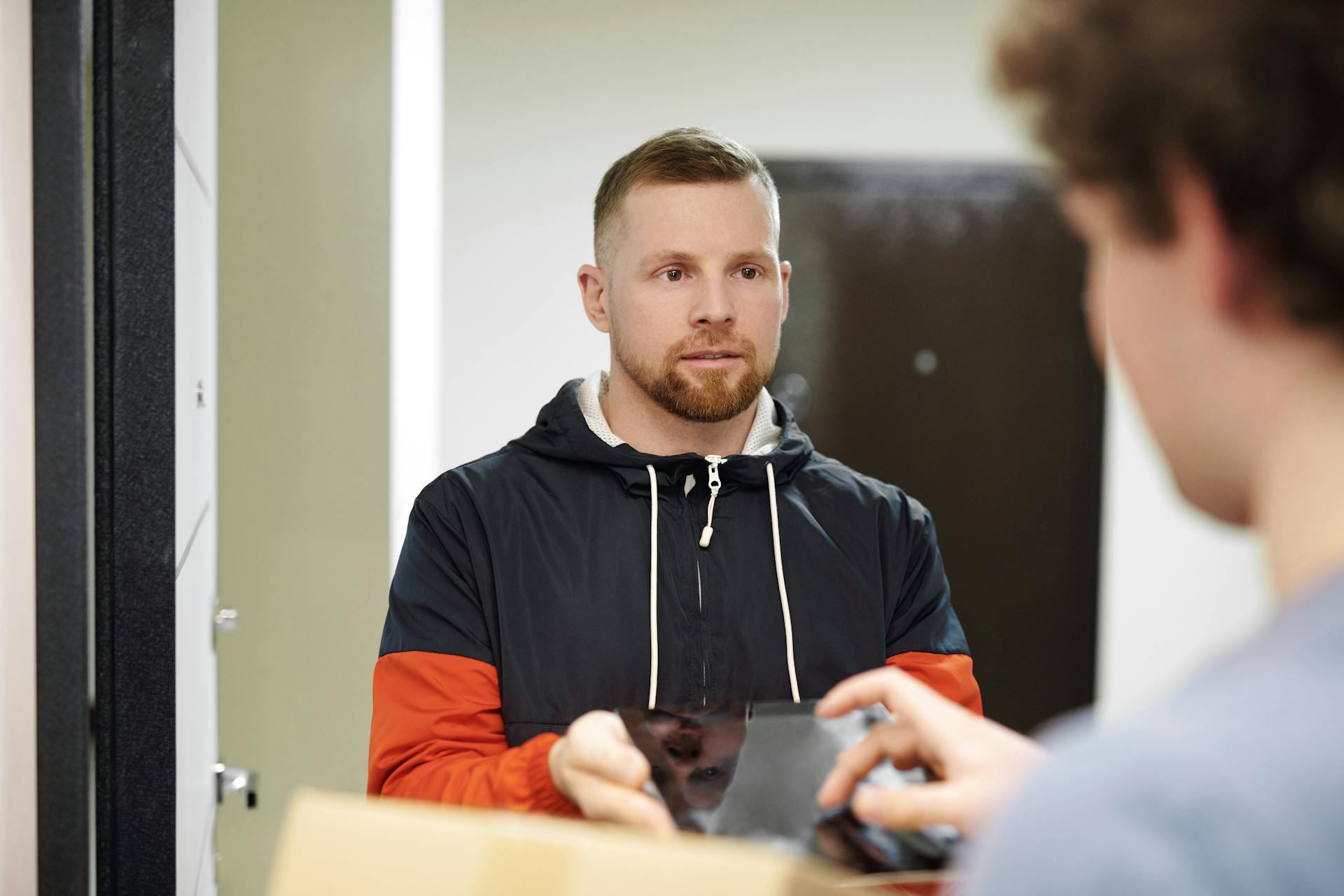 A delivery driver in a hoodie receiving a package indoors, focusing on customer interaction and modern lifestyle.