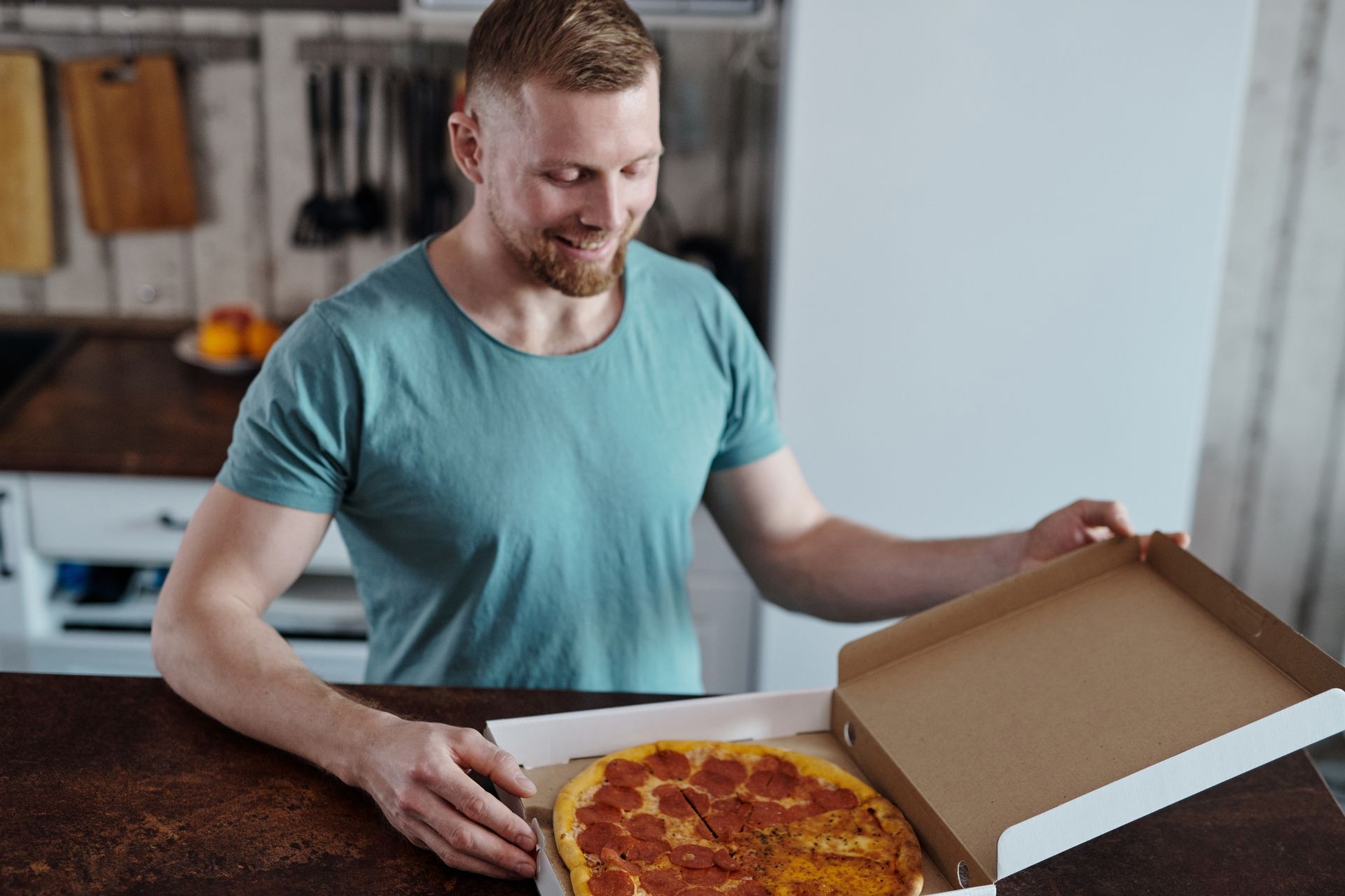 Delighted man opens a pizza box at home, enjoying a delicious meal delivery.