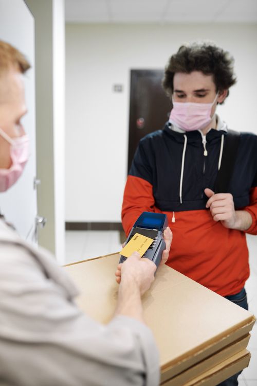 Free A man receives a pizza delivery while maintaining safety measures with contactless payment. Stock Photo