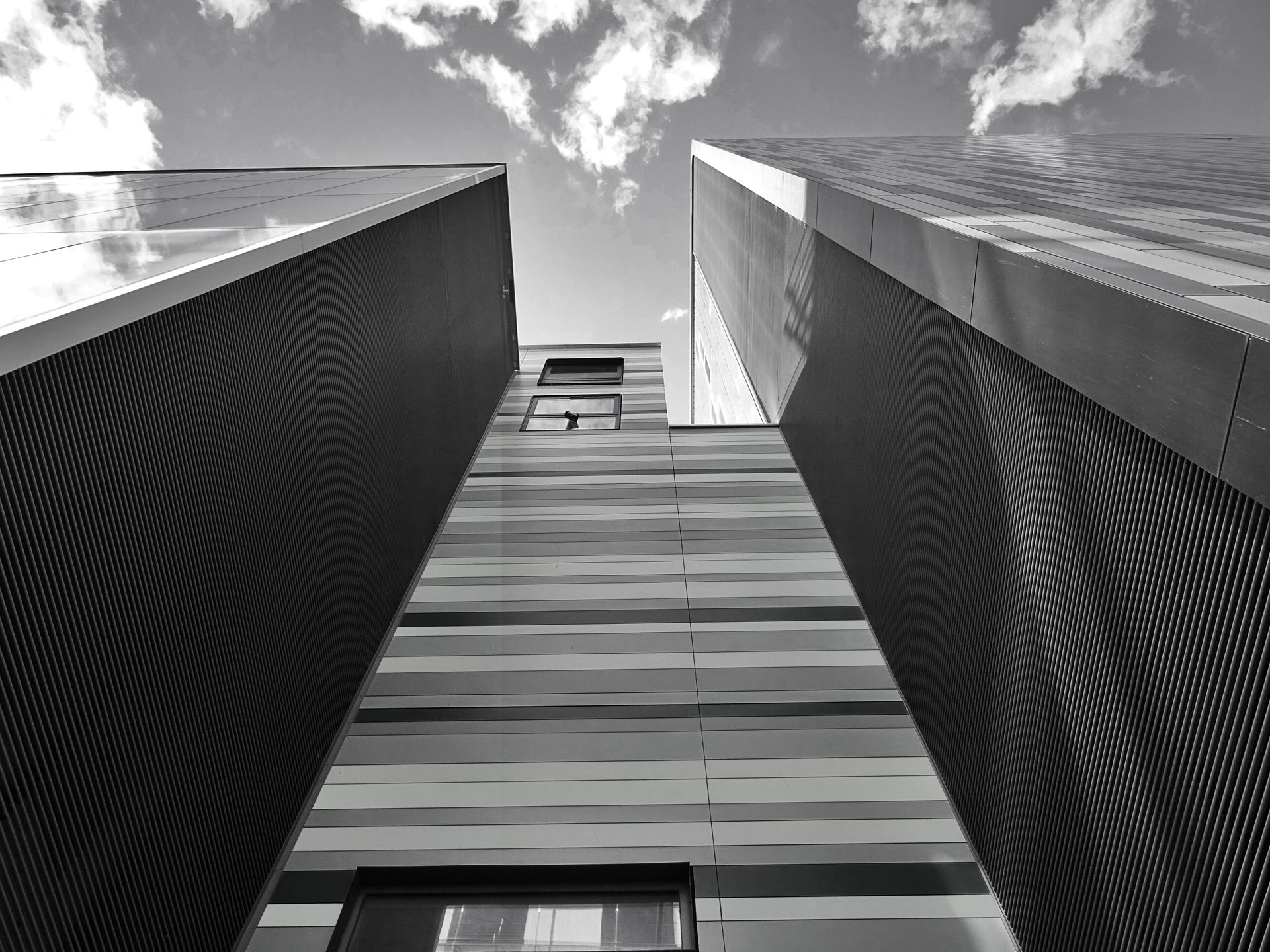 Low-angle black and white photo capturing modern skyscraper architecture with dramatic clouds.