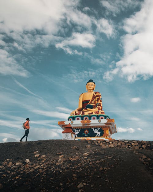 Unrecognizable traveler near ancient Buddha statue located in mountainous valley