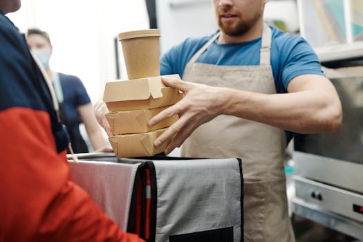 A delivery worker handing over food packages in a busy kitchen setting.