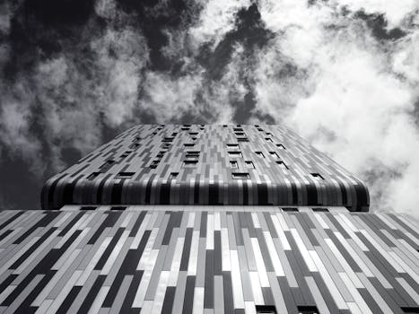 低角度单色视角下的现代摩天大楼立面，映衬着戏剧性的多云天空