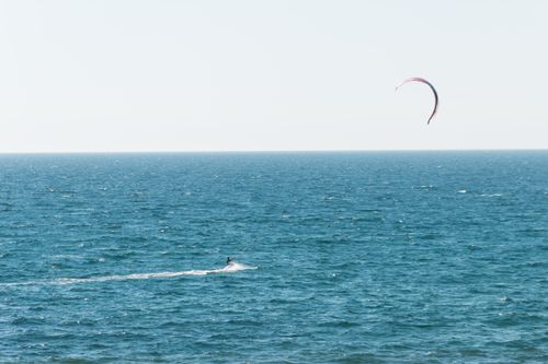 Free Faceless person doing parasailing while sliding on water surface of endless ocean under light blue cloudless sky Stock Photo