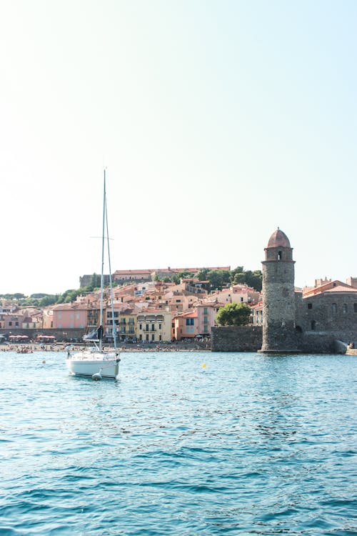 Light blue cloudless sky above sailboat in ocean near coast of cozy touristic town