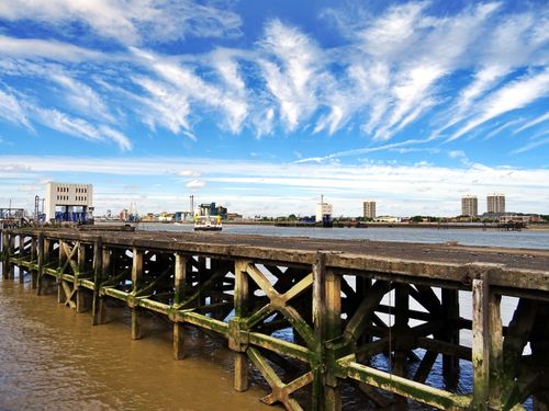 Free Wooden pier leading to a city skyline with dramatic clouds against a blue sky. Stock Photo