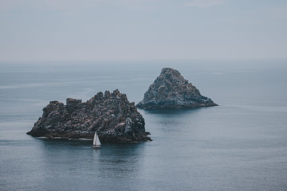 Cloudless sky above small white sailboat next to hills in high silent ocean in daylight