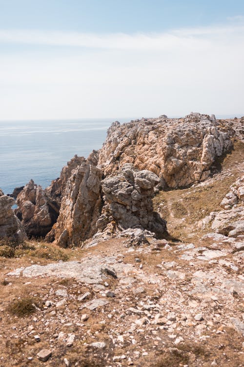 Picturesque view of stony terrain with rocky mountains on coast of calm sea water under cloudy sky in daytime