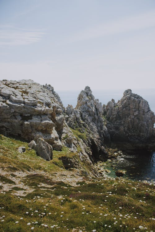 Picturesque landscape of rough rocks and green sloppy hill near sea on sunny day