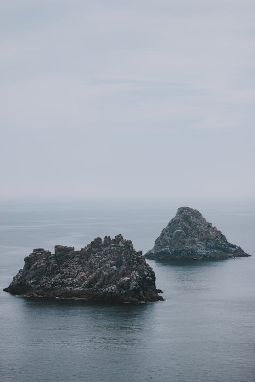 Scenic seascape with rough rocks located in calm water of sea on cloudy day