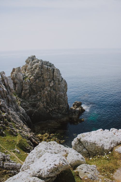 Free Majestic scenery of green hill with rough rocks near calm sea with turquoise water on sunny day Stock Photo