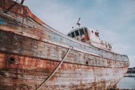 Abandoned weathered fishing boat on shore near calm sea in port on sunny day