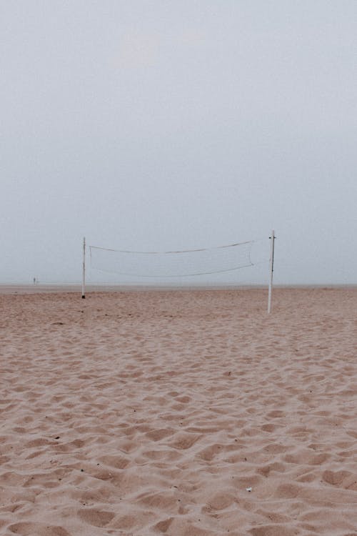 Peaceful scenery of sandy seashore with old volleyball net on background of gray sky