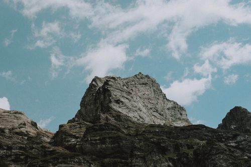 Free Low angle of rough stony mountain range with green moss against cloudy blue sky Stock Photo