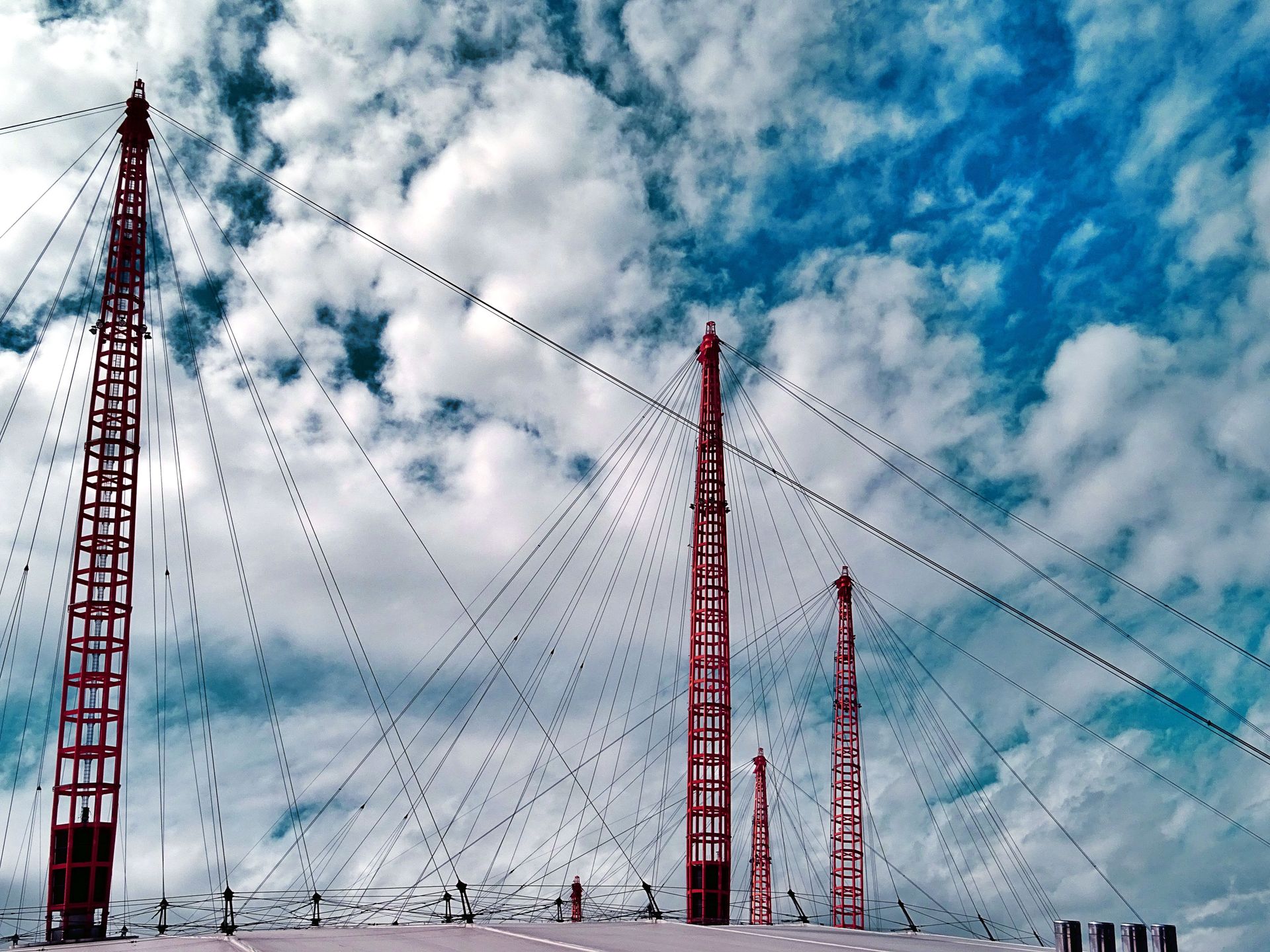 Close-up view of suspension bridge cables and towers against a vibrant cloudy sky.