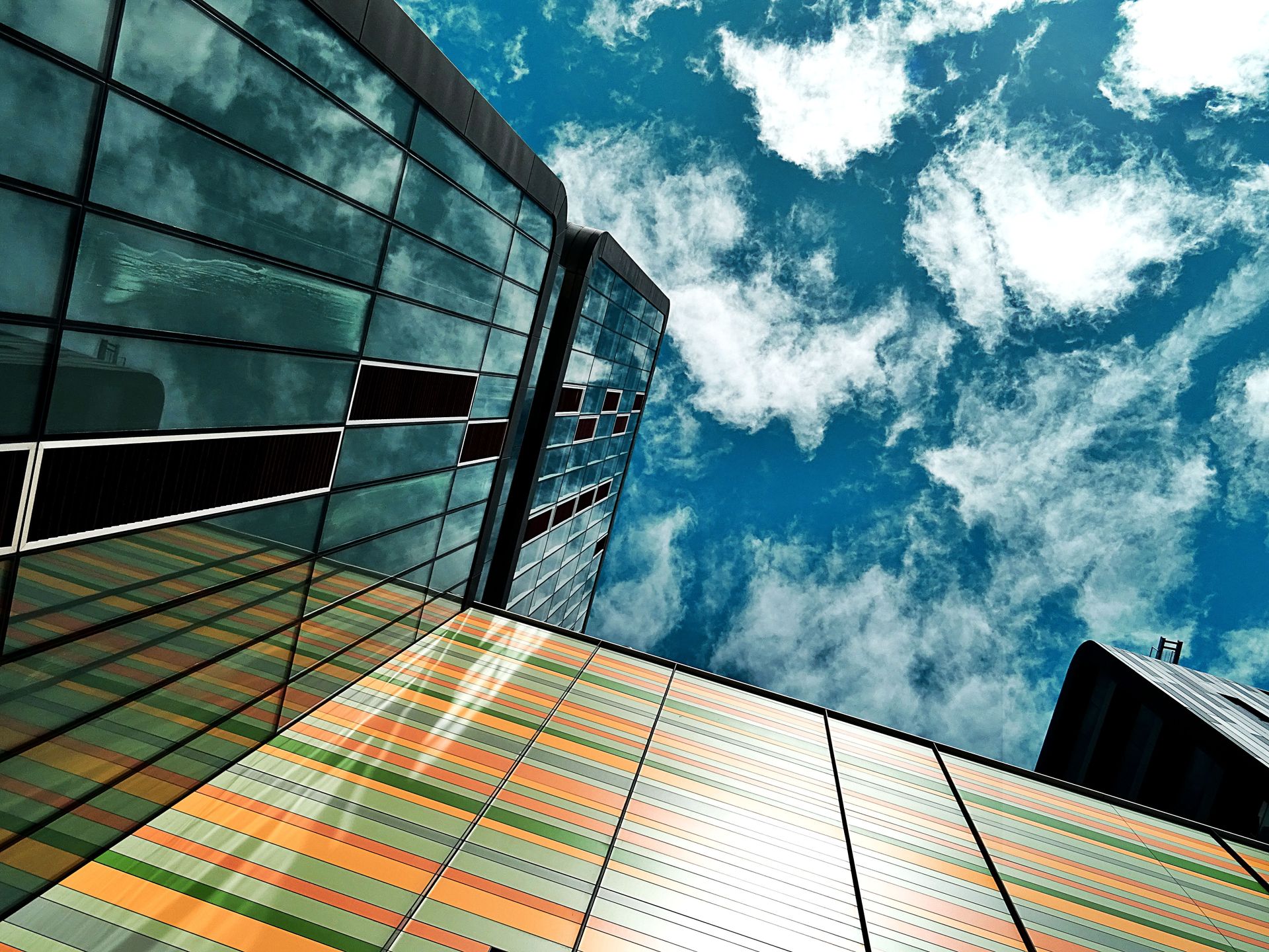 Modern skyscraper with glass panels and colorful facade reflecting a vibrant blue sky.
