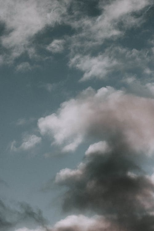 From below of white and gray fluffy cumulus and cirrus clouds floating in blue sky