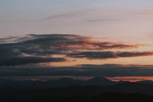 From below of gray clouds floating in sky over wild mountainous valley at sunset