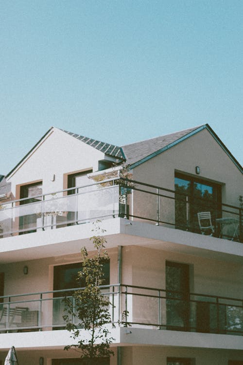 Low angle corner of modern residential house with glass balconies and sharp roof against cloudless blue sky