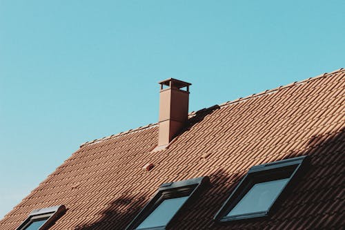 Free From below of chimney and attic windows on tiled roof of modern residential house against cloudless blue sky Stock Photo