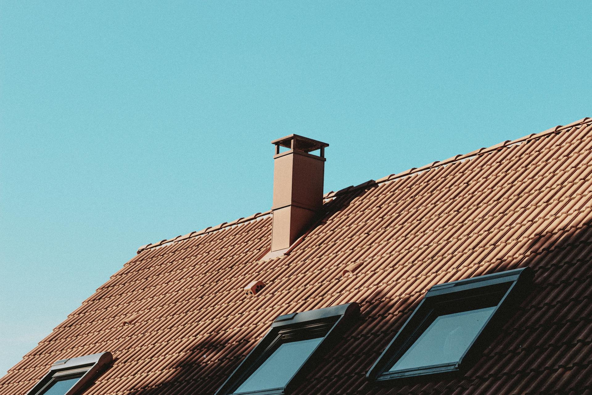 From below of chimney and attic windows on tiled roof of modern residential house against cloudless blue sky