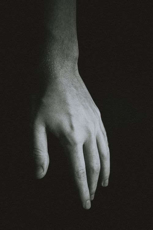 Free Black and white of crop faceless male with hanging hand against dark background Stock Photo