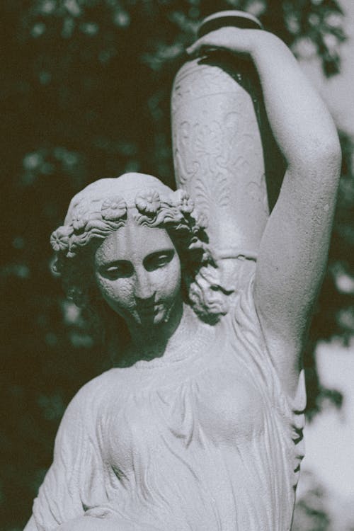 Antique figure of young female in dress with hair tied up carrying vase on shoulders on blurred background