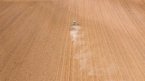 Contemporary tractor leaving long traces and smoke while plowing brown plantation in daylight