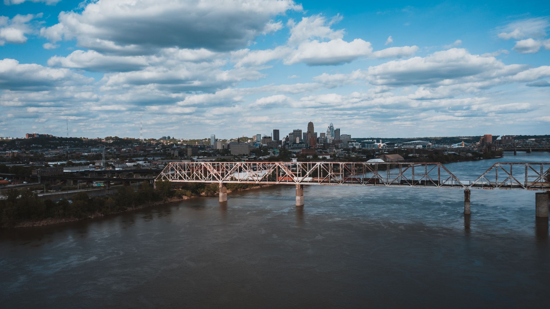 Picturesque scenery of city embankment and bridge crossing river against cloudy sky on summer day