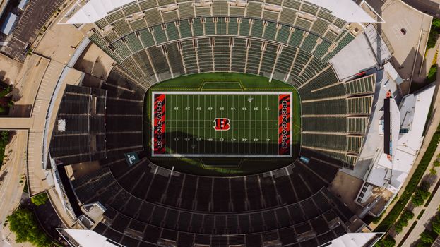 Top view of empty tribunes and American football stadium with white lines and emblem on sunny day