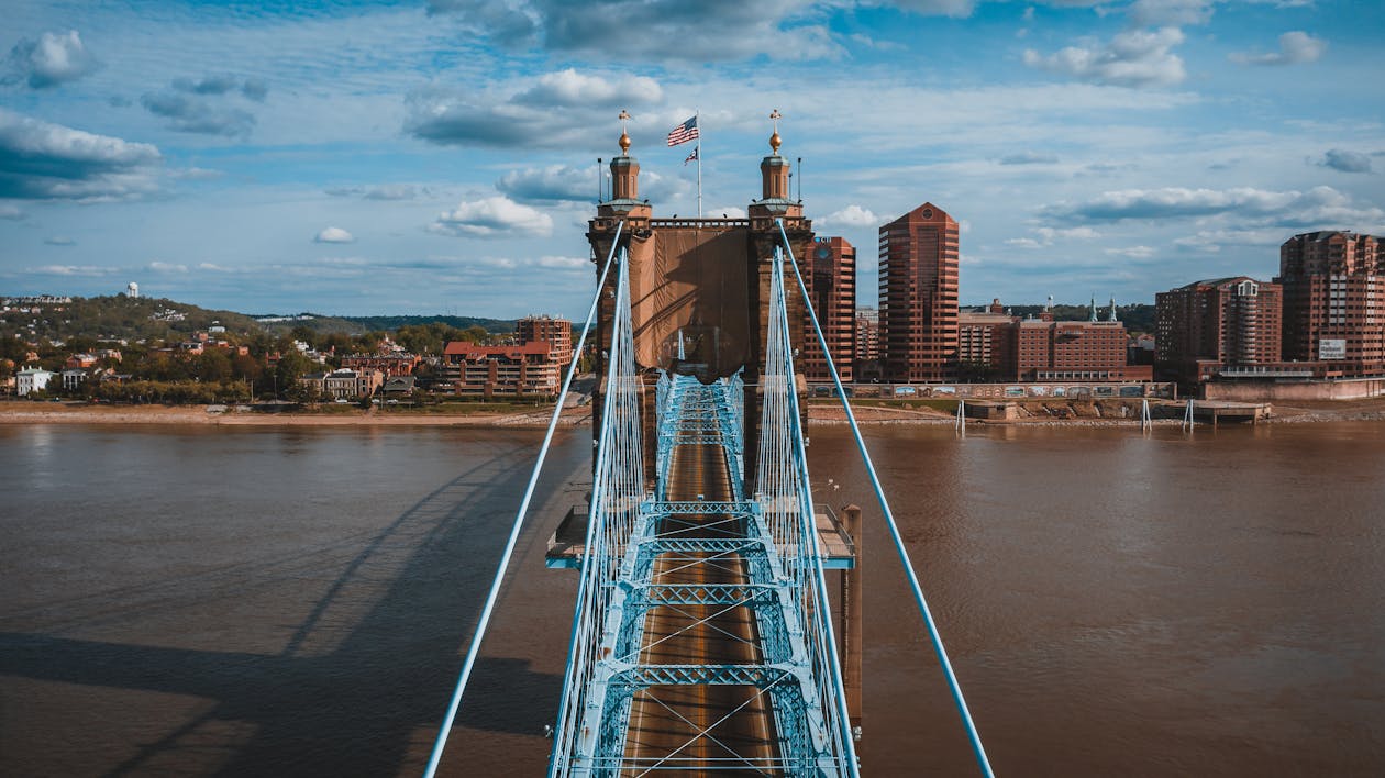 Picturesque view of ancient John Roebling Suspension Bridge crossing muddy river against cloudy sky on sunny day