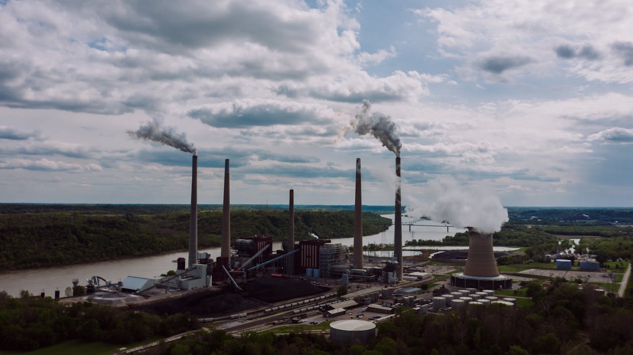 Free Air pollution by smoke coming out of factory chimneys located near river against cloudy sky on summer day Stock Photo