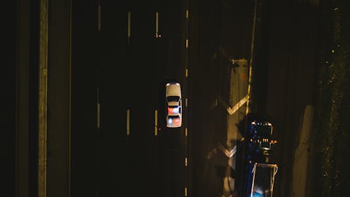 From above of police cruiser with flashing lights driving on asphalt road along dimly illuminated street at night