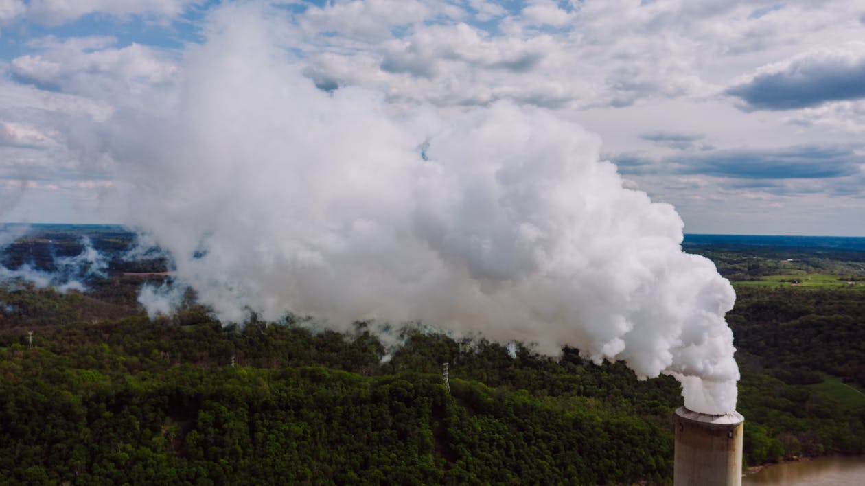 Free Thick chimney smoke under cloudy sky above greenery trees Stock Photo