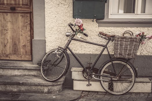 A vintage bicycle with a wicker basket filled with flowers, parked against a textured wall on a street.