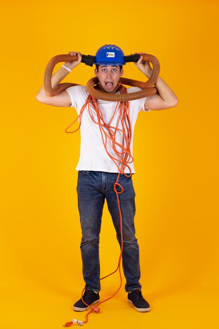 Man In Hard Hat Tangled In Extension Cord And Vacuum Cleaner Hose