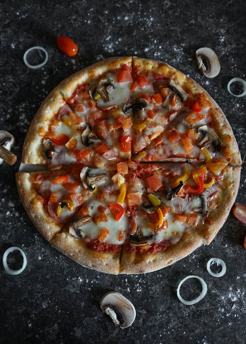 Top view of tasty pizza with crispy edges and tender texture decorated with colorful pepper and tomato slices on melted mozzarella cheese