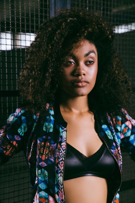 Young stylish arrogant black female with Afro hairstyle in underwear and ornamental blouse looking away near grid fence