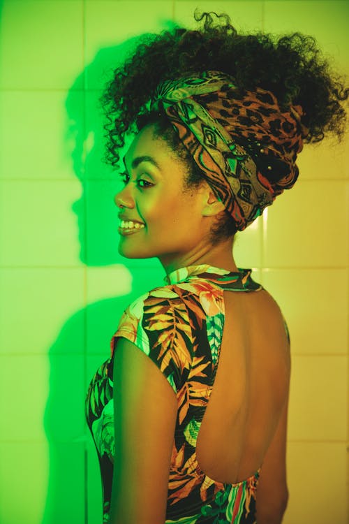 Back view of cheerful African American female in stylish wear with creative hairstyle and makeup looking away near colorful wall