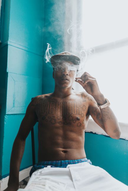 A tattooed man smoking in a vibrant blue indoor space, creating an artistic vibe.