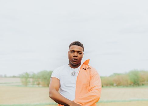 Portrait of a stylish man wearing an orange jacket standing confidently in a wide open field.