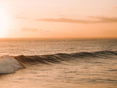 Free A tranquil view of the ocean waves at sunset in Bali, Indonesia, showcasing a picturesque orange sky. Stock Photo