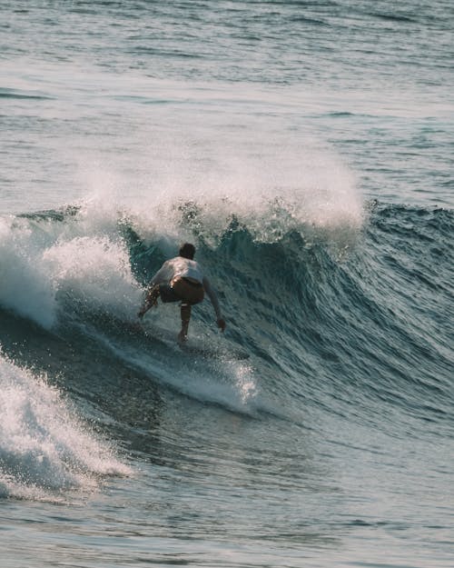 Photo of a Man in a White Long Sleeve Shirt Surfing on Sea Waves