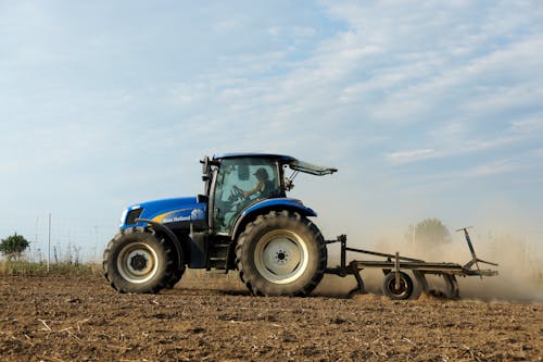 Free Blue Tractor on Brown Field Under White Clouds Stock Photo
